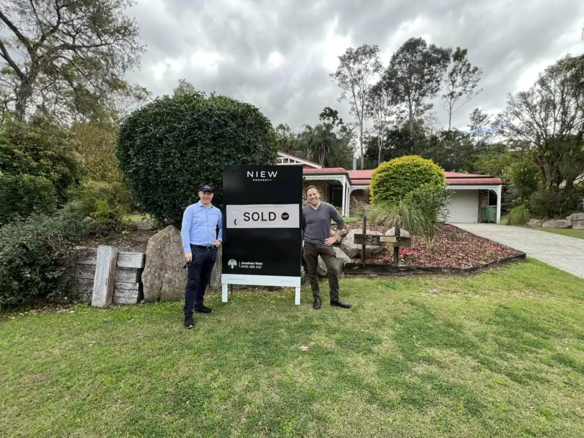 Sam Price, Brisbane buyer’s agent, with a client beside the SOLD sign outside the home he bought for them
