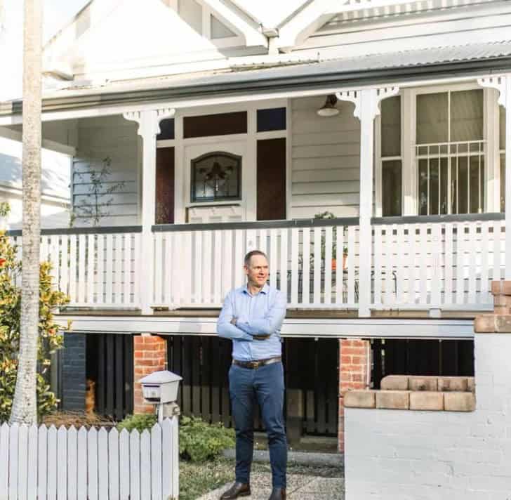 Sam Price, Brisbane Buyer's Agent, outside a Queenslander home with a white picket fence