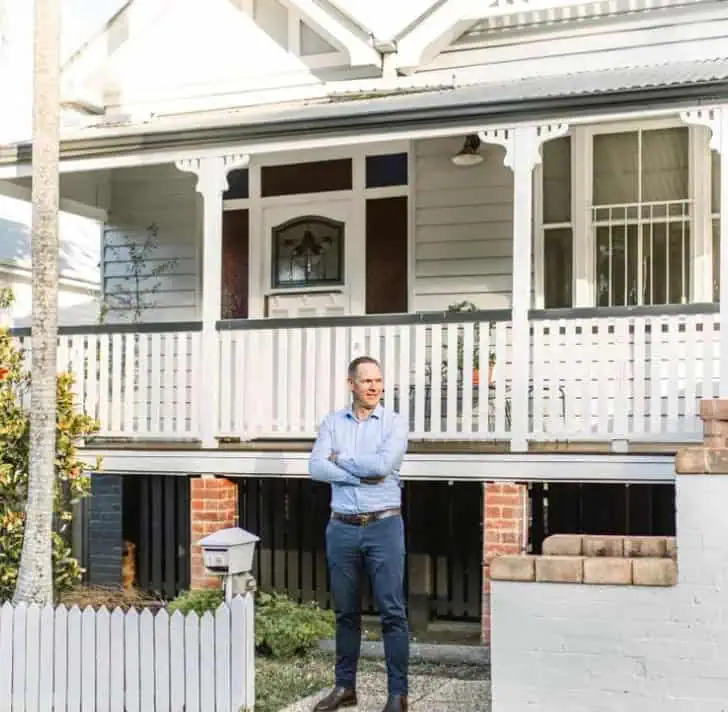 Sam Price, Brisbane Buyer's Agent, outside a Queenslander home with a white picket fence